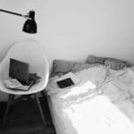 Laptop na krześle w jasnej, monochromatycznej sypialni z łóżkiem