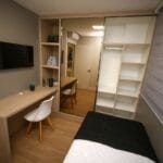Minimalistyczna sypialnia w bloku z biurkiem, lustrem i regałem