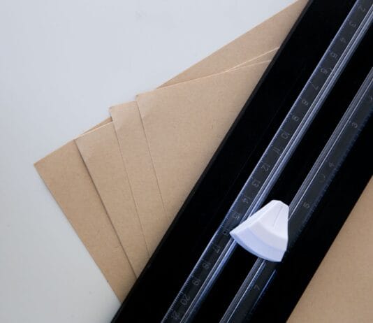 Kostka introligatorska z kości, plastiku czy teflonu? Porównanie do pracy z papierem Brązowe arkusze papieru z linijką i nożykiem introligatorskim