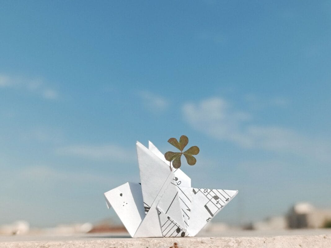 Papierowy żuraw origami z koniczyną na tle błękitnego nieba