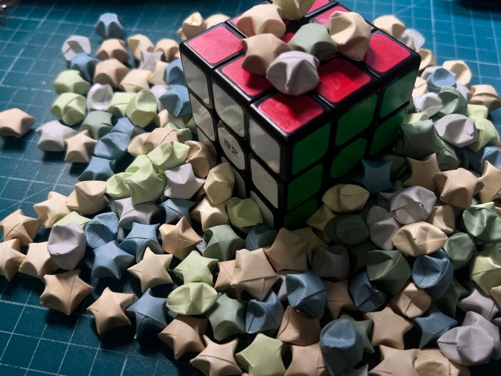 Kostka Rubika otoczona pastelowymi gwiazdkami origami na niebieskiej macie
